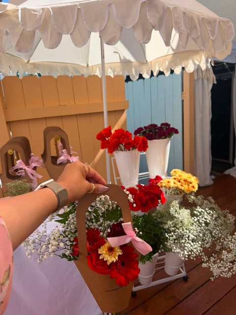Person arranging colorful flowers in vases under a beige canopy at a flower shop display stand