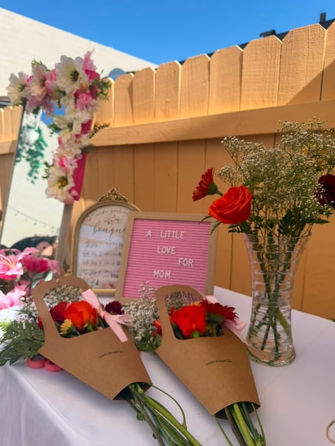 Mothers Day display featuring flower bouquets, a pink sign reading A Little Love for Mom, and decorative signage on a wooden fence background