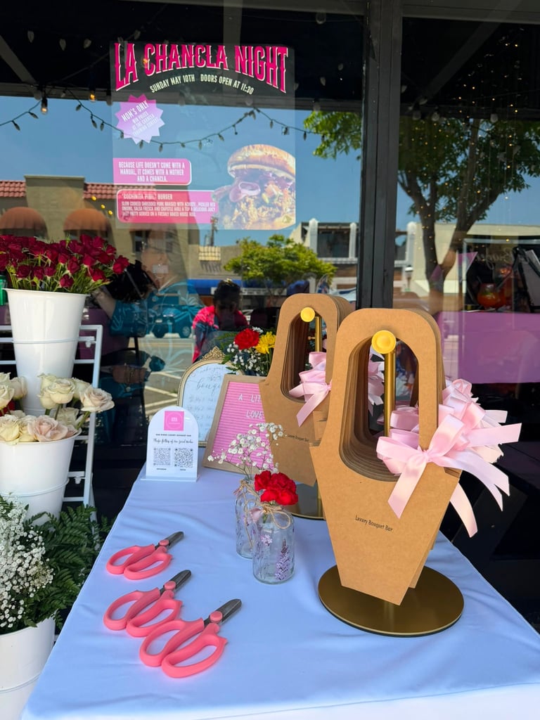 Outdoor storefront display for La Chancla Night event featuring cardboard cactus decorations, pink flowers, red flip-flops, and promotional signage